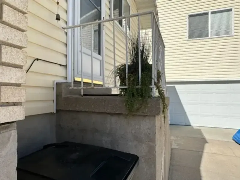 Old painted metal handrail rusting at its fixings on a raised concrete entry landing
