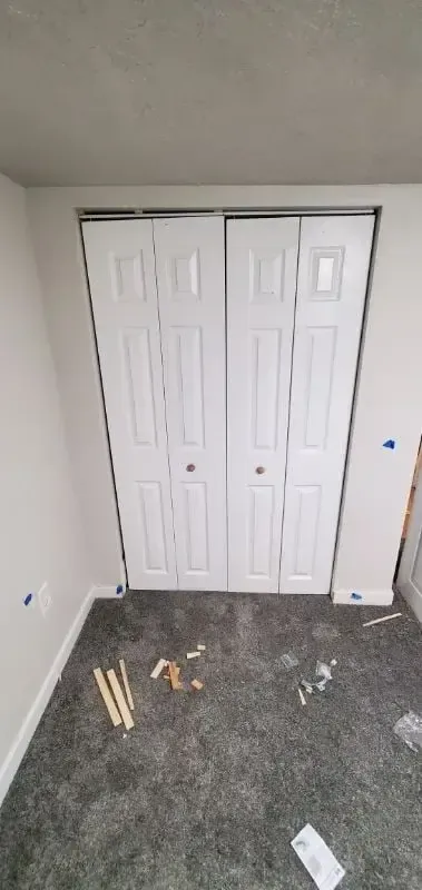 Newly installed white six-panel bi-fold closet doors in a carpeted bedroom