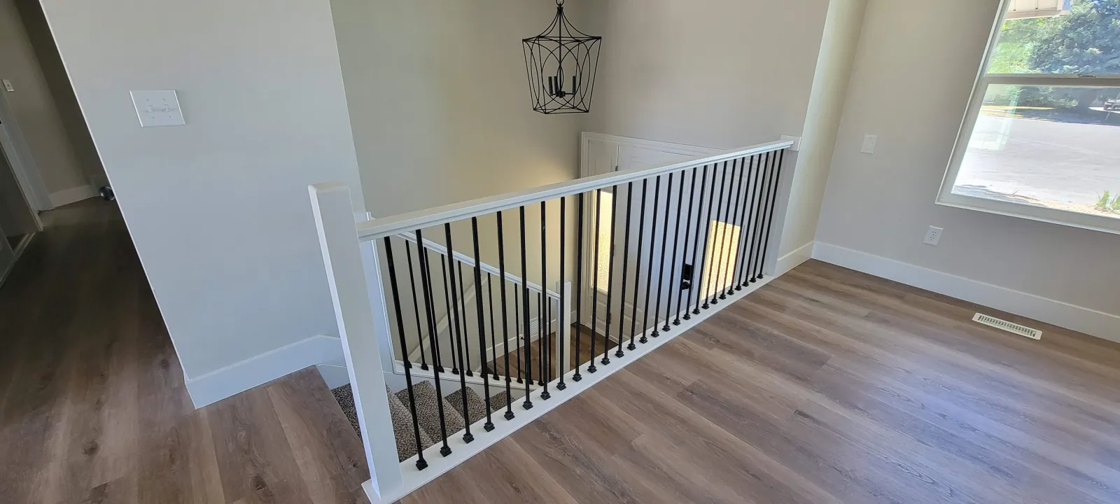 Interior stair railing with black metal balusters and white newel posts beside a wood-look floor landing