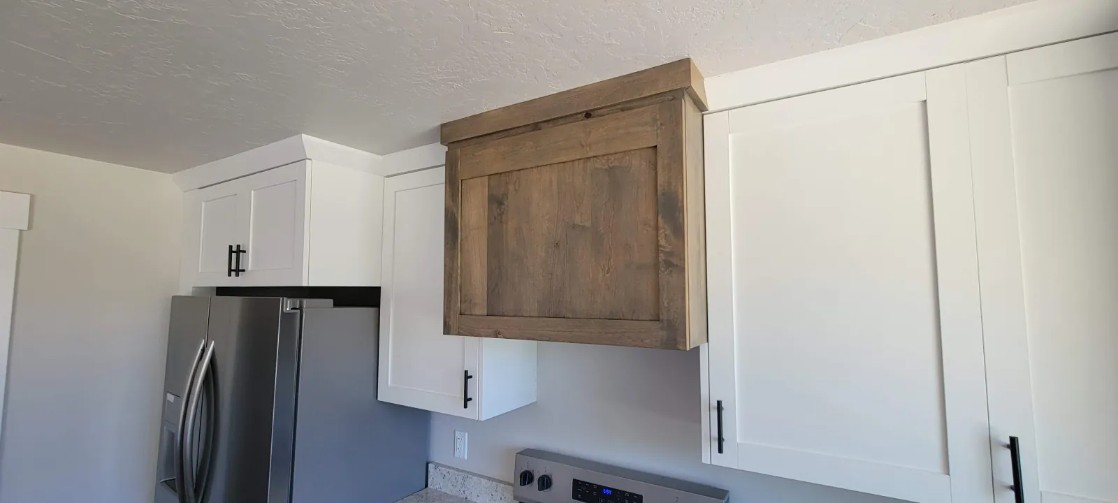 Kitchen with white cabinets, a stainless refrigerator and a stained wood cabinet above it