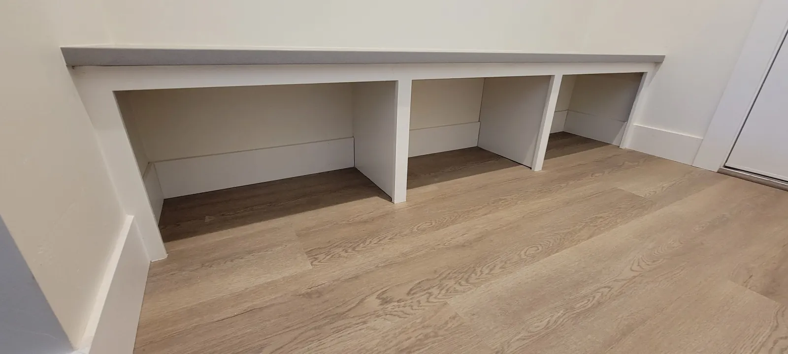 Long white built-in bench with open storage cubbies along a hallway wall