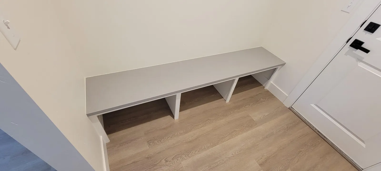White built-in mudroom bench with open cubbies on a wood-look floor