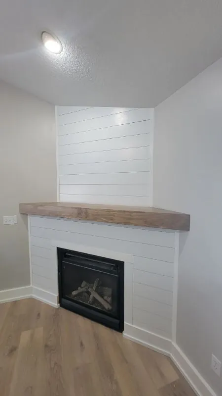 Corner fireplace finished in white shiplap with a wood mantel
