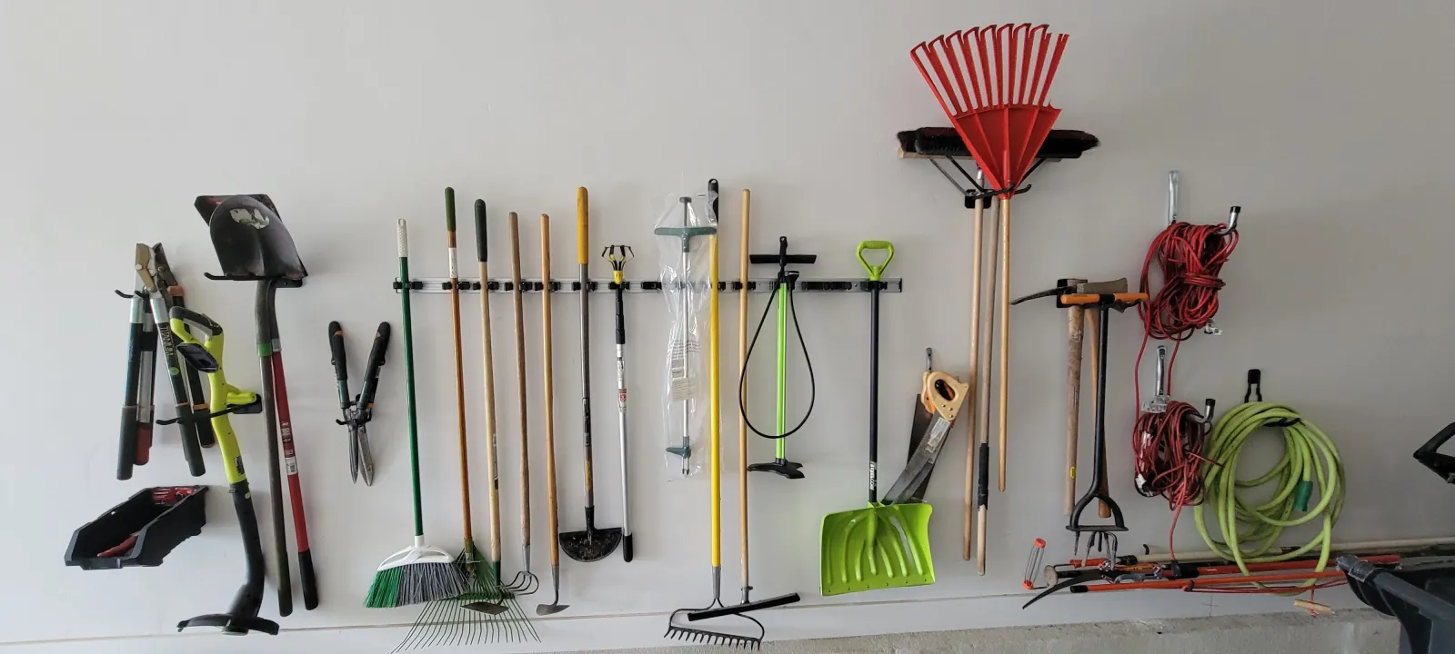 Garage wall with rakes, shovels and hand tools hung on a mounted storage rail
