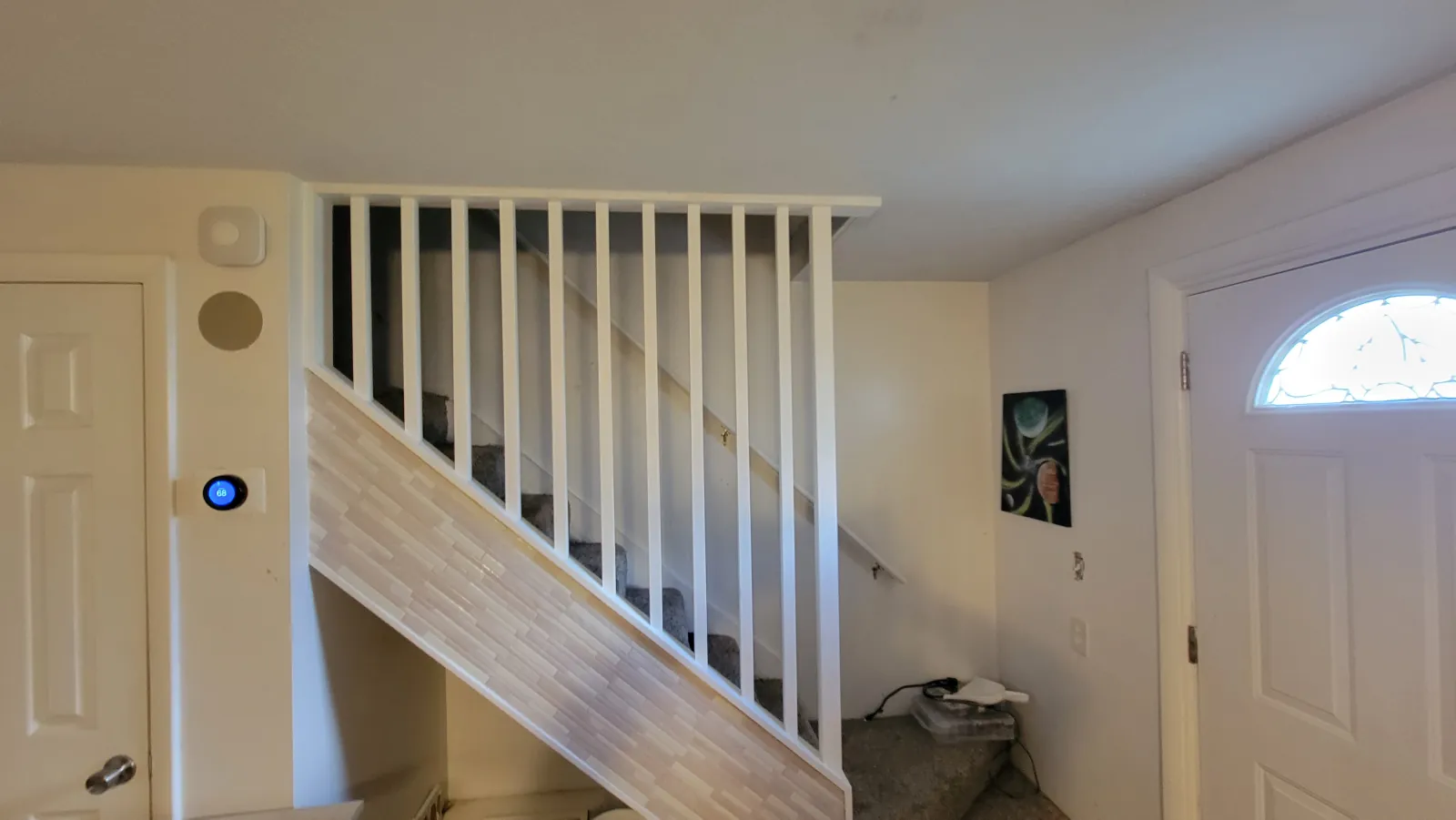 Interior staircase with white balusters next to a front door with an arched window
