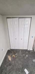 Newly hung white bi-fold closet doors with trim offcuts still on the carpet