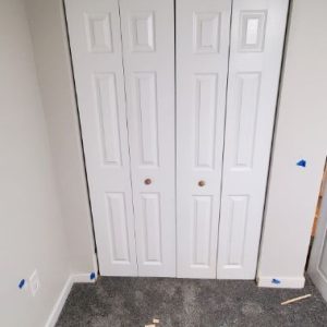 Newly hung white bi-fold closet doors with trim offcuts still on the carpet